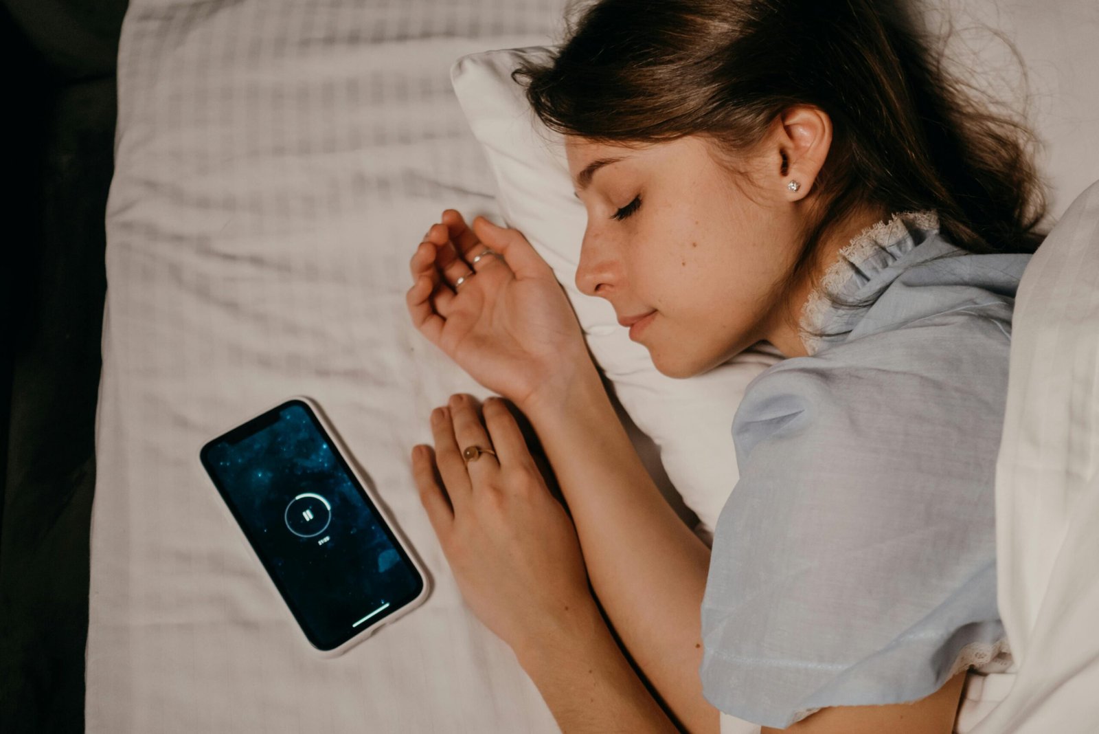 A woman peacefully sleeps in bed with a smartphone beside her, illustrating modern bedtime habits.